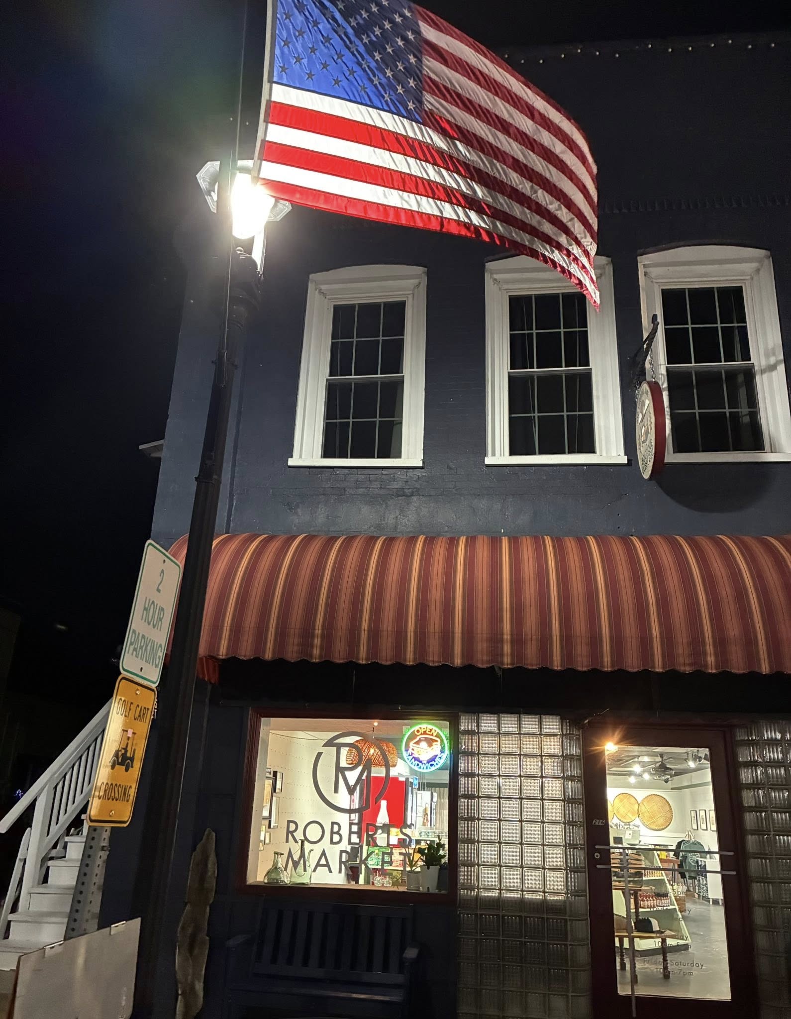 Roberts Market storefront lit up at night beneath an American flag